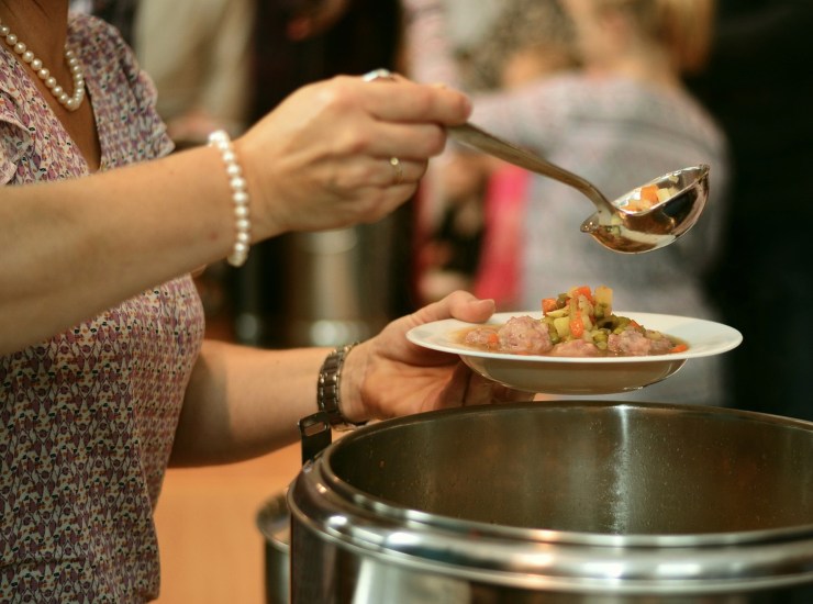 Donna serve il cibo da un pentolone al piatto